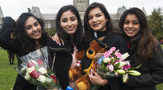 Four students pose for photos holding bouquets