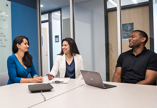 Three staff members sit at a table talking