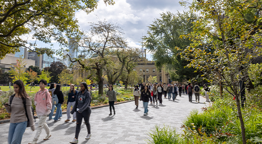a crowd of people walking along a front campus pathway