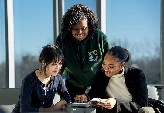 three students look at a book together