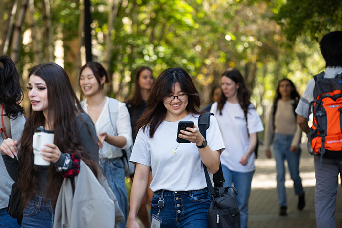 Students walk outside and one is looking at her phone and smiling