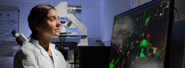 A woman in a lab coat looks at a computer screen