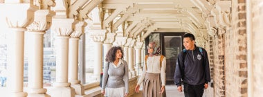 Three students walk while talking to each other