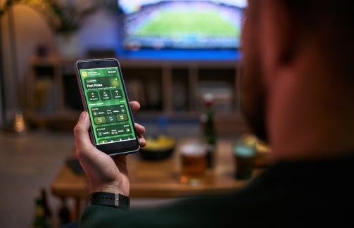 man gambles on a cellphone while watching baseball on tv in his living room