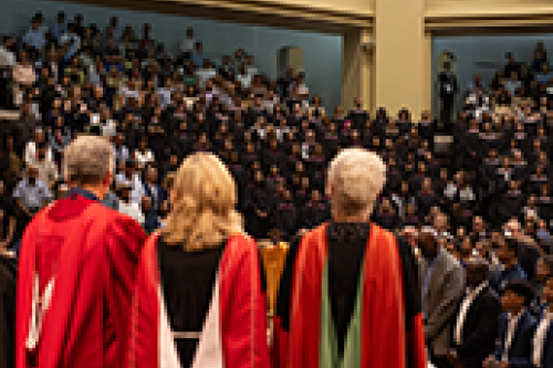 Three people stand on stage and a crowd is in front of them