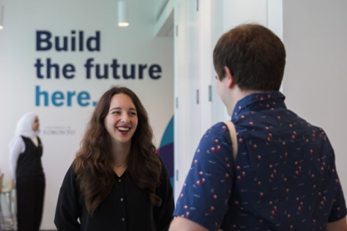 Two people talk in front of sign that reads build the future here