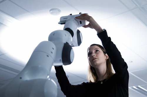 A woman reaches up to adjust a robotic arm