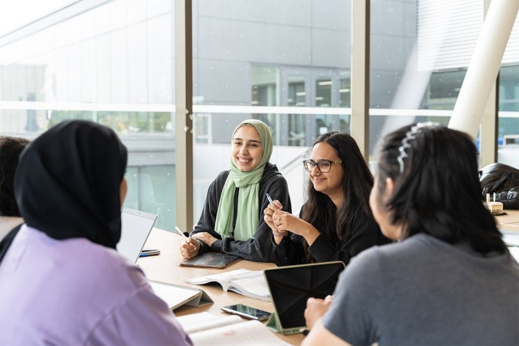 students sit around a table together smiling at UTM