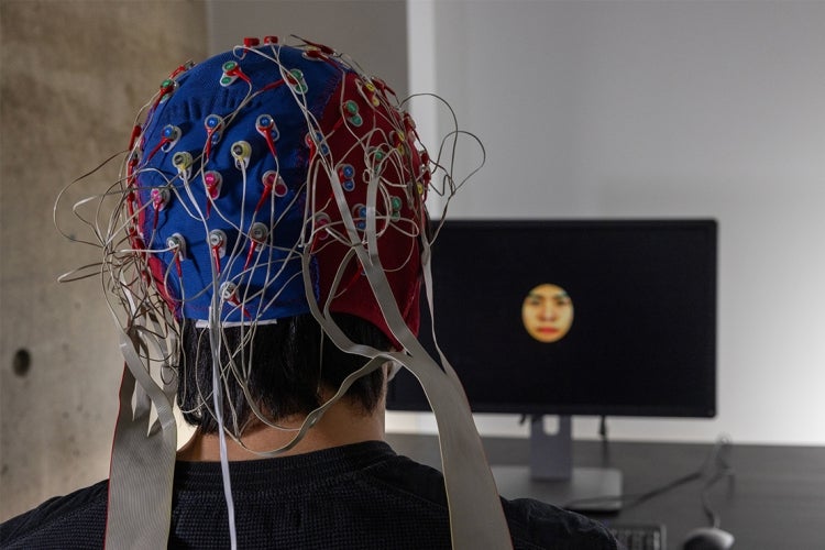 test subject wearing a device on his head while watching a screen with a face on it
