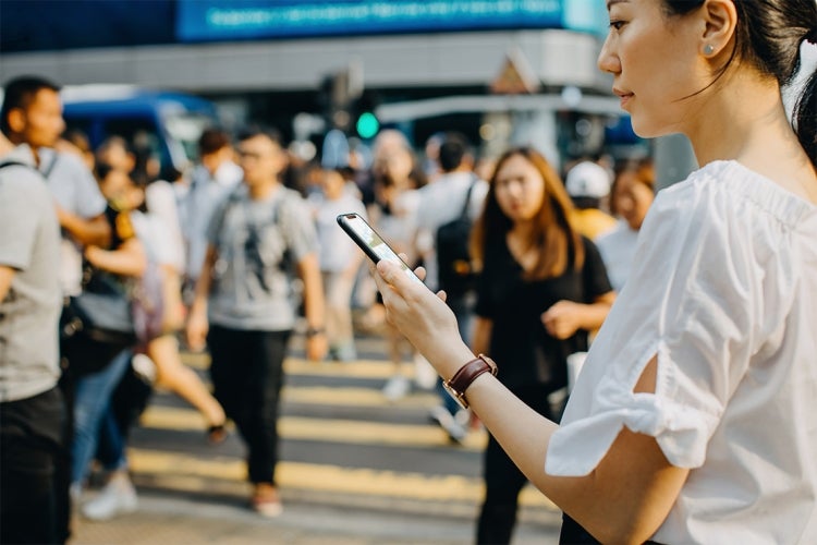woman looks at stock information on her smartphone with a busy downtown street in the background