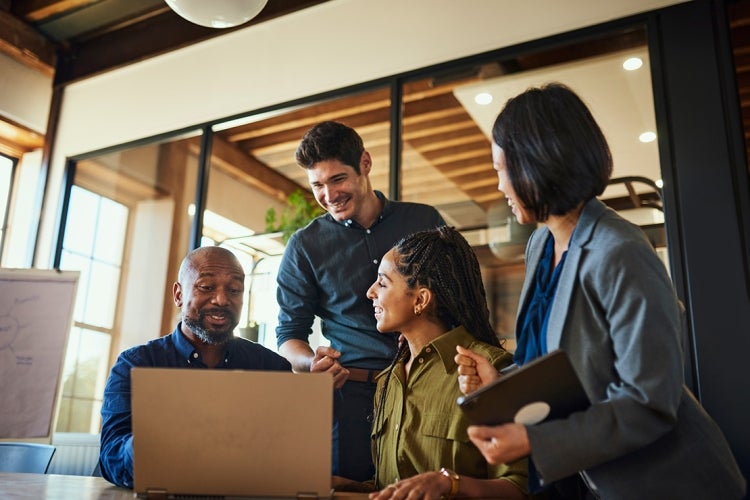 office workers huddle and laugh around a laptop
