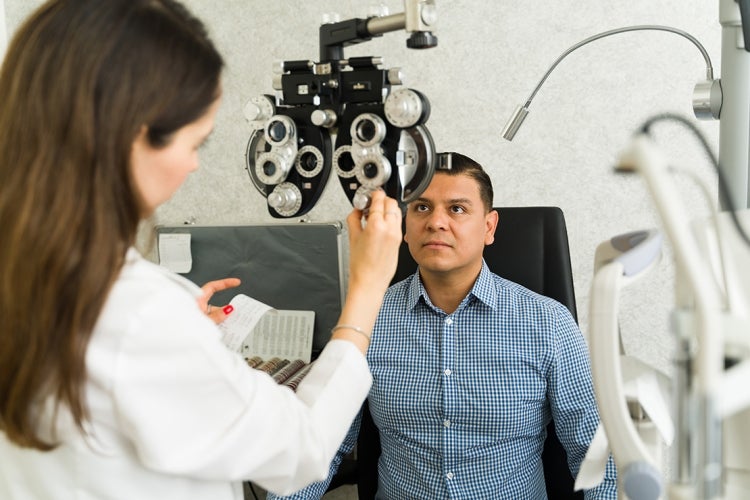 a hispanic man sits for an eye exam with an optometrist