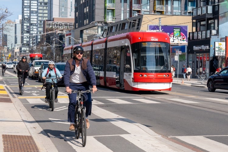 cyclists in Toronto bike along a bike lane downtown. There is a streetcar in the background