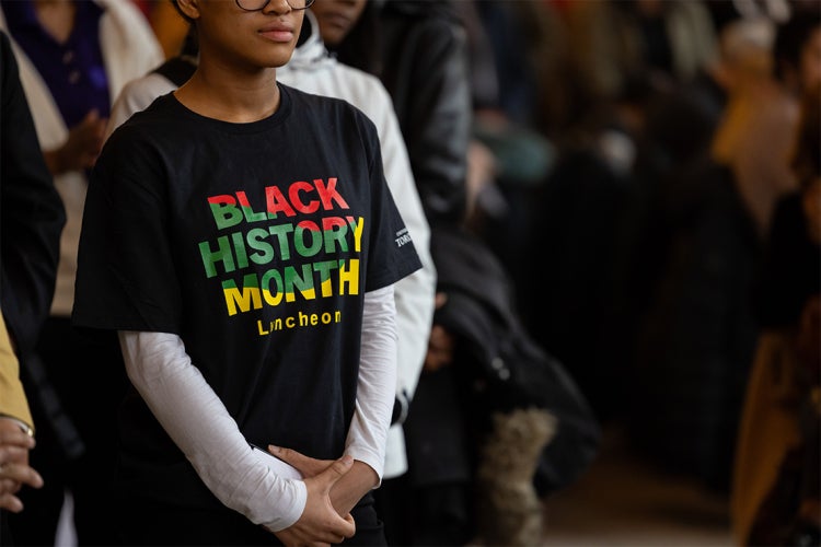 Black university student wearing a T shirt that reads "Black History Month Luncheon"