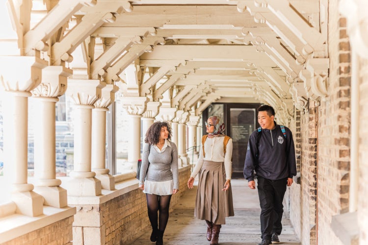 three students walking through a walkway in the University College quad at the University of Toronto