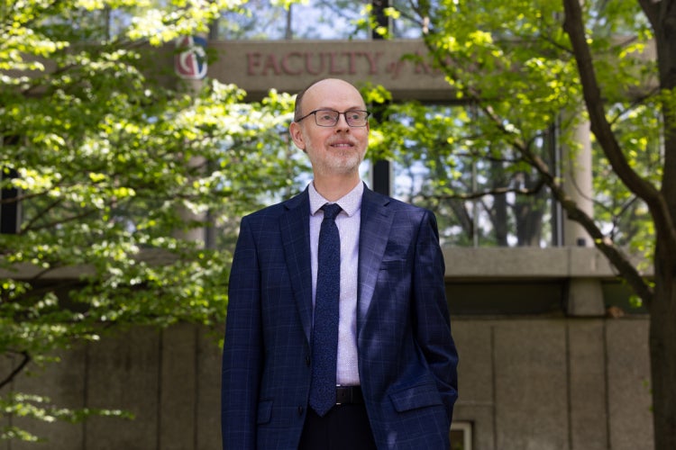 Ryan McClelland stands in front of trees and the Faculty of Music sign on the St. George campus
