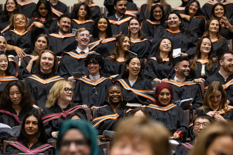 graduands are seen lauging and smiling while they sit in convocation hall during a graduation ceremony