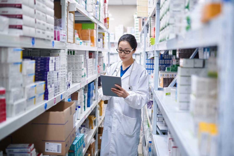 a female pharmacist checks inventory on pharmacy shelves