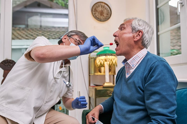 senior citizen gets a coronavirus rapid test administered at home by a doctor