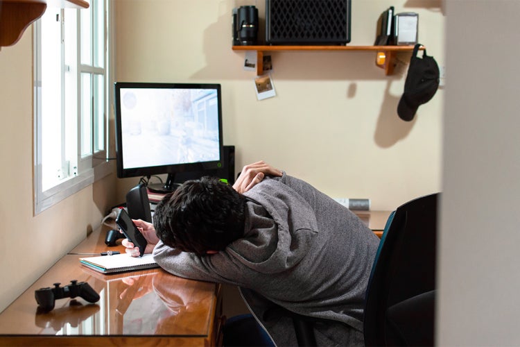 a student lazily looks at his cell phone while in front of a desktop computer