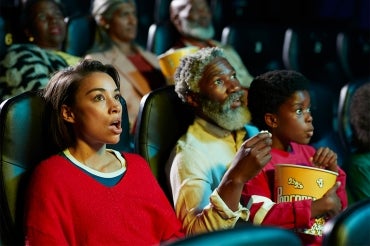 A mother, father and child have a look of surprise on their faces while watching a movie at a theatre
