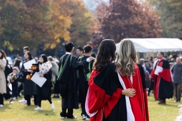 two female graduates are seen from the back as they take a selfie on front campus after their convocation ceremony