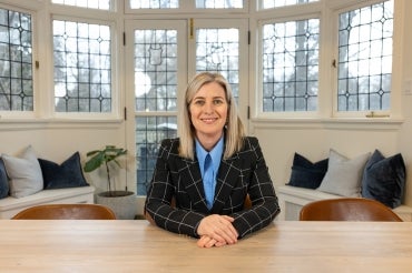 Melanie Woodin sits at desk in front of a bay window