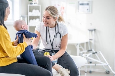 A mother holds up her infant for a nurse to examine