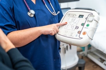 medical doctor hold up a defibrilator and points to the instructions on the unit