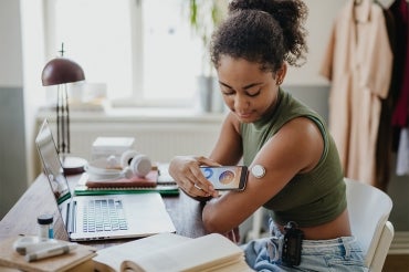 A young woman uses a smartphone to read her glucose monitor on her arm