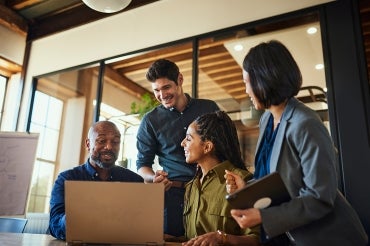 office workers huddle and laugh around a laptop