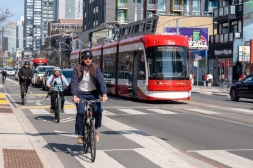 cyclists in Toronto bike along a bike lane downtown. There is a streetcar in the background