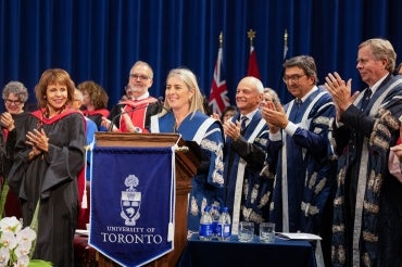 Melanie Woodin at podium surrounded by previous presidents of the university during her installation ceremony