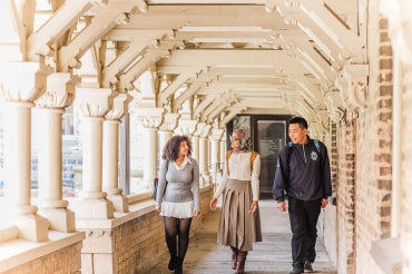 three students walking through a walkway in the University College quad at the University of Toronto
