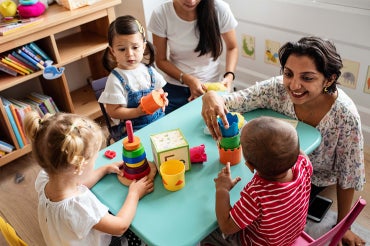 A woman engaging with 3 toddlers in a day care setting