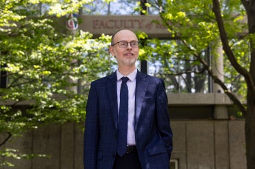 Ryan McClelland stands in front of trees and the Faculty of Music sign on the St. George campus