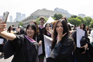 graduating students smile while taking a selfie outside of convocation hall 
