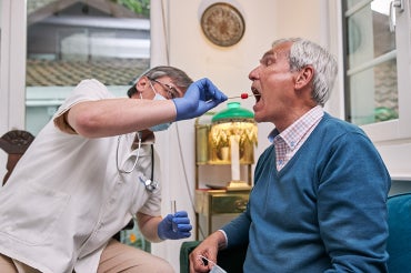 senior citizen gets a coronavirus rapid test administered at home by a doctor