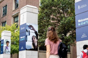 a student walks past signage at the University of Toronto main gate