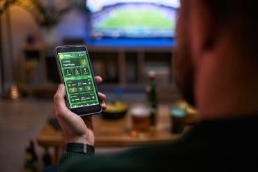 man gambles on a cellphone while watching baseball on tv in his living room
