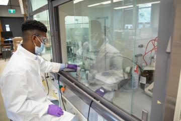 Gaius St. Marie works in a lab using a fume hood behind glass