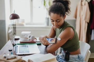A young woman uses a smartphone to read her glucose monitor on her arm