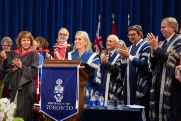 Melanie Woodin at podium surrounded by previous presidents of the university during her installation ceremony