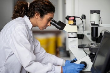 a woman looks through a microscope in a university of toronto lab