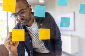 man writing on post it notes posted to a glass wall