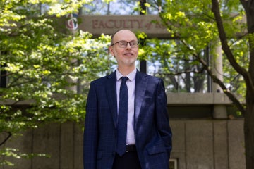 Ryan McClelland stands in front of trees and the Faculty of Music sign on the St. George campus