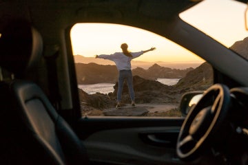 woman looking out at sunset outside of a car alone