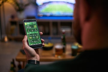 man gambles on a cellphone while watching baseball on tv in his living room