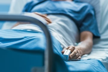 Person lying down in a hospital bed with a monitor on their finger