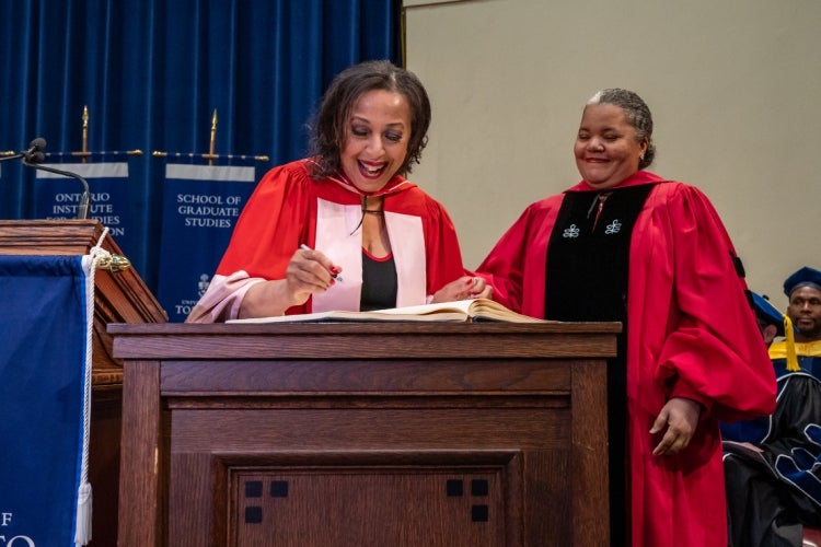 Rosemary Sadlier signs the book of honorary degree recipients while Dean Erica Walker looks on